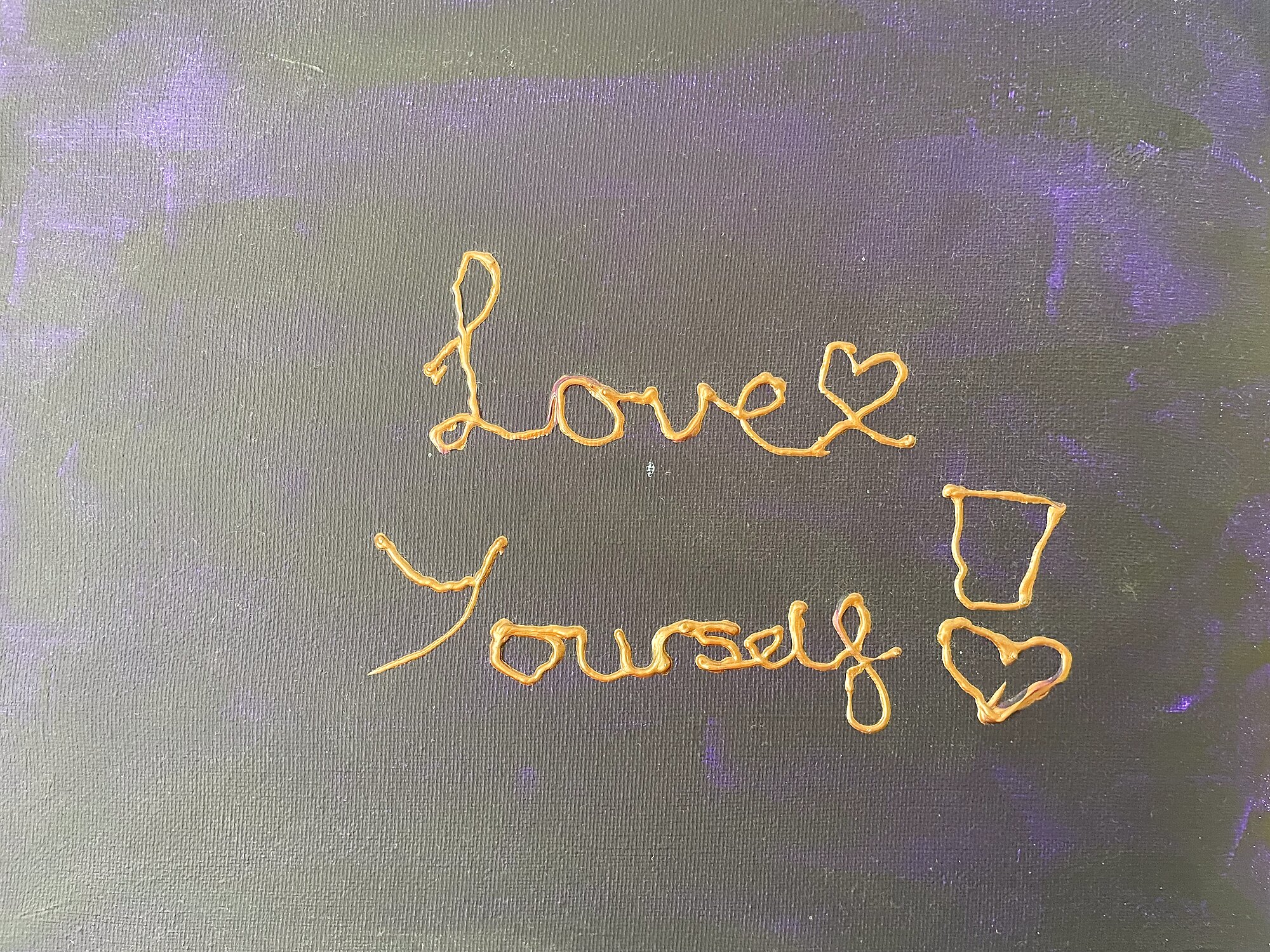 A painting Luna made - gold cursive on dark canvas reading 'Love Yourself' with a small heart
